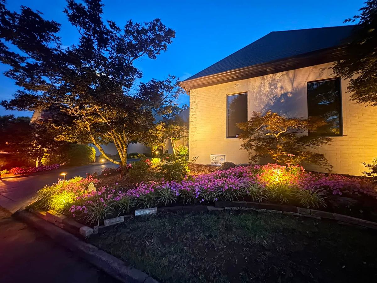 Landscape lighting illuminating a flower bed and home entry at dusk
