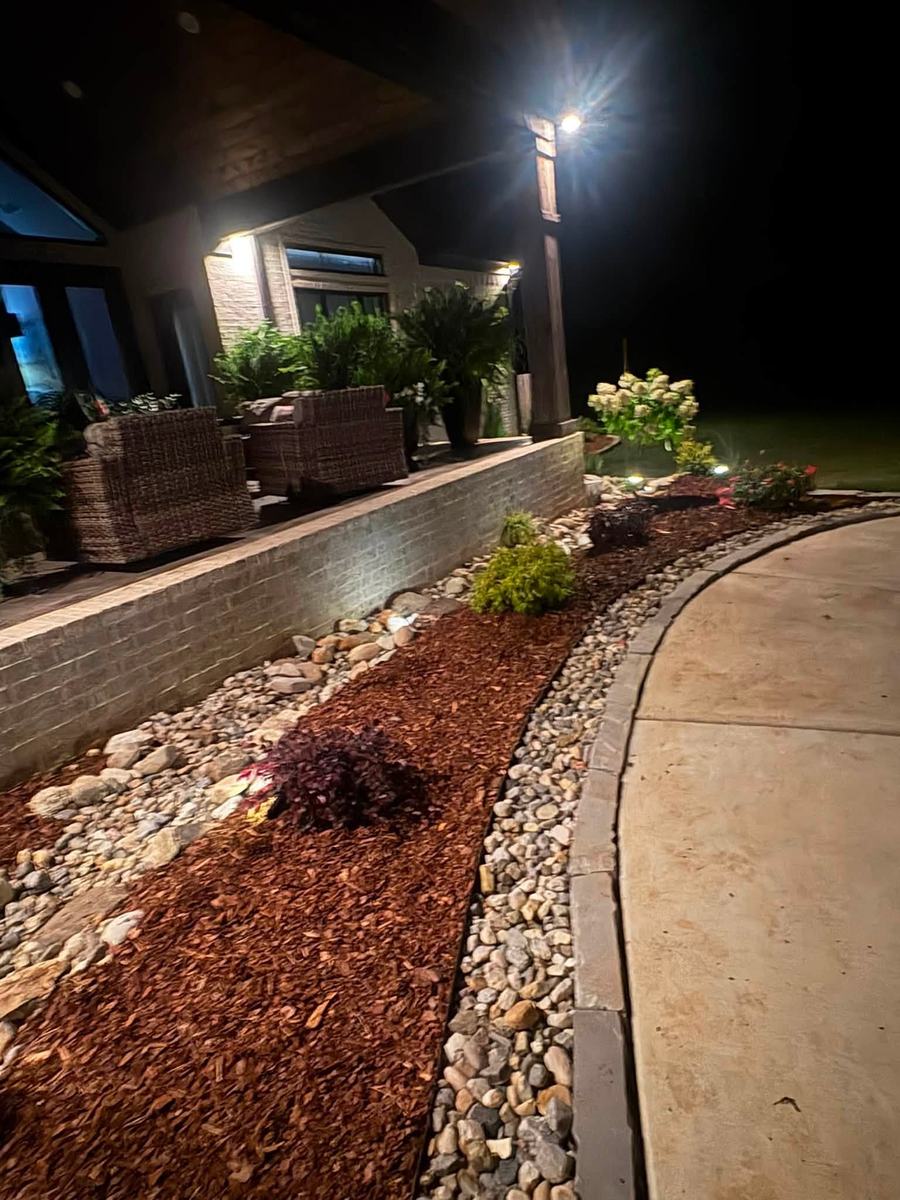 Rock bed and mulch along a driveway lit up at night near a patio